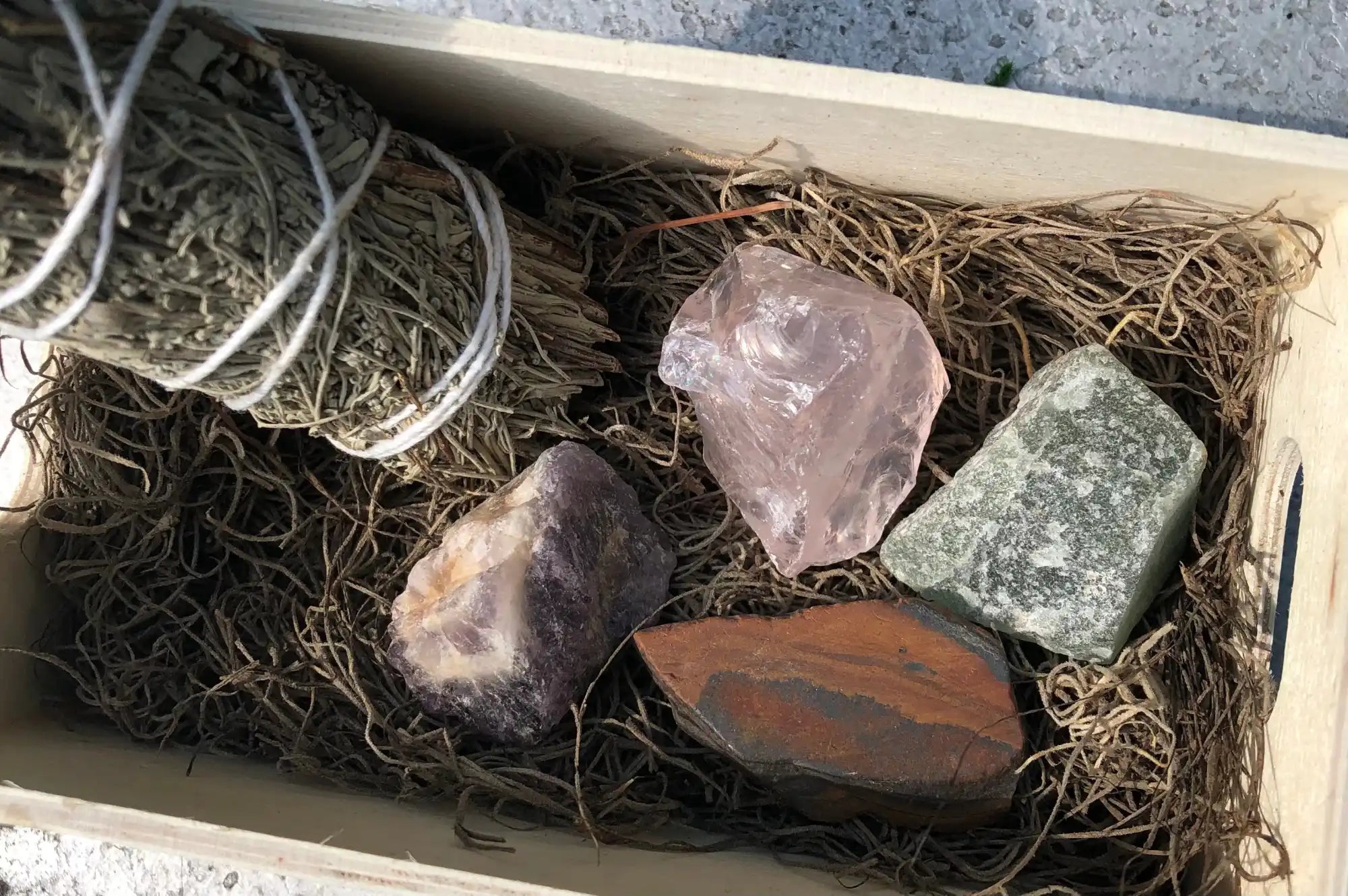 A wooden box containing sage bundles and various raw crystals.